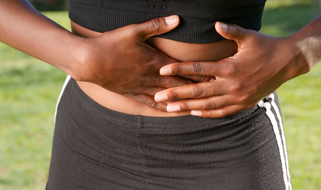 Mulher com as mãos sobre a barriga estufada, sinal típico de inchaço