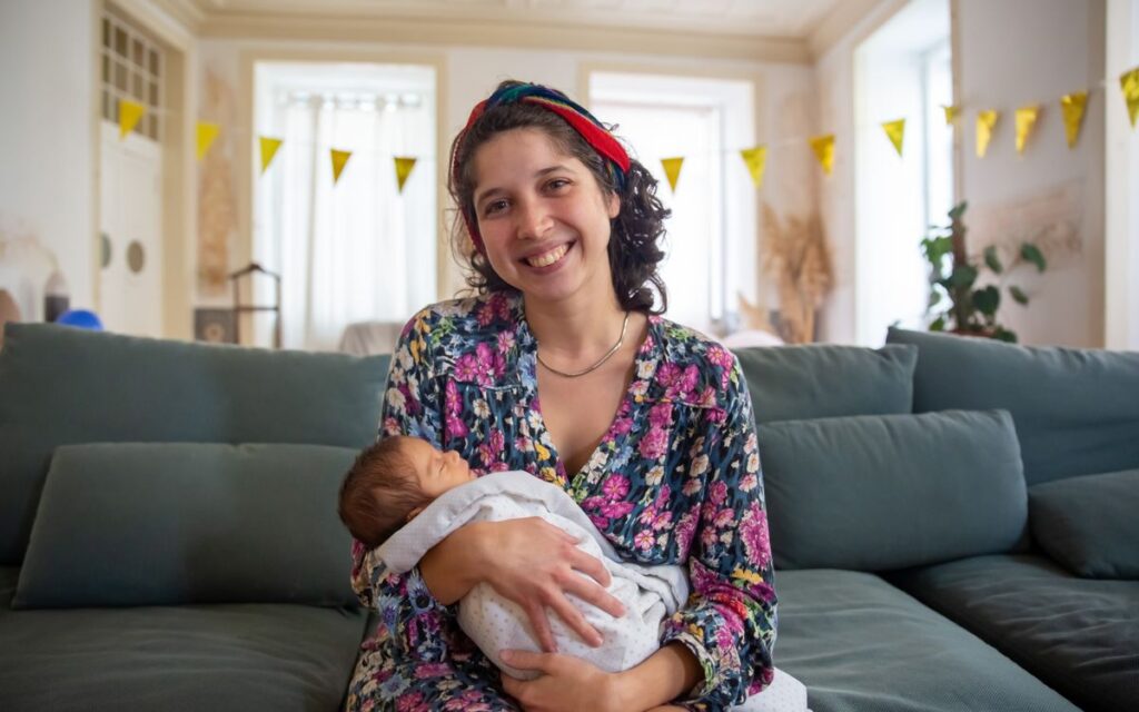 Mae sorrindo segurando o bebe recem-nascido em casa
