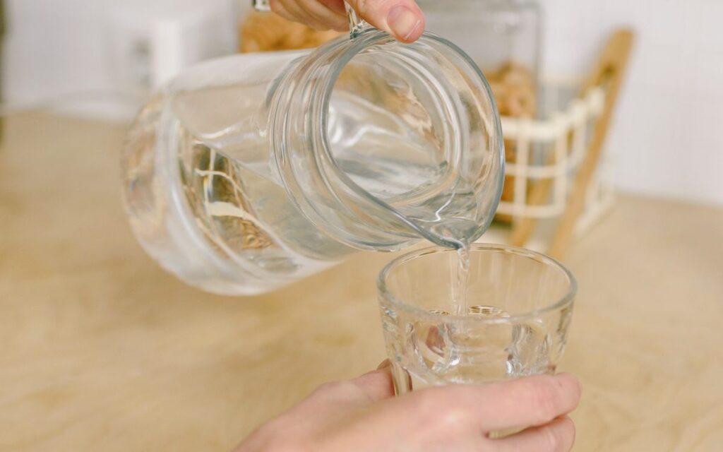 Maos servindo agua de uma jarra em um copo